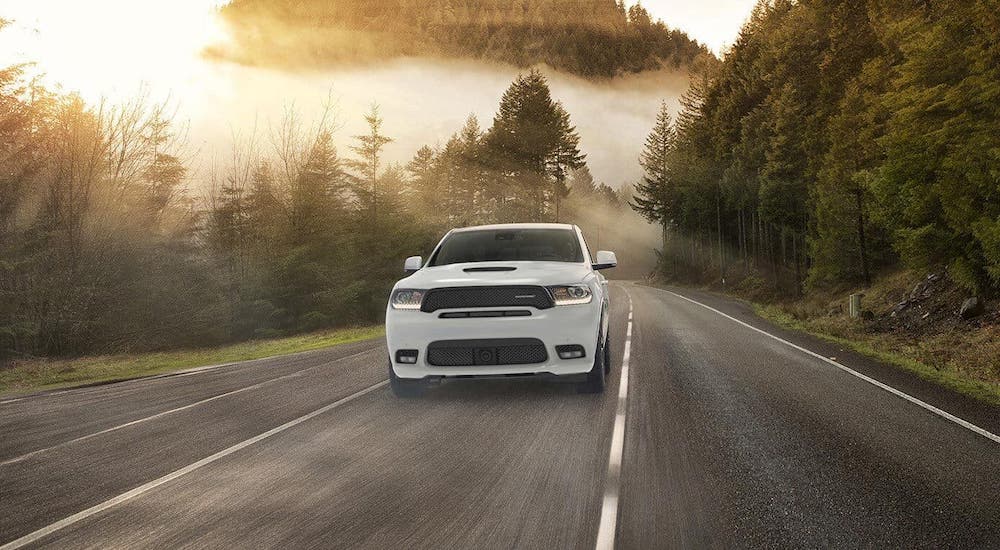 A used SUV for sale, a white 2019 Dodge Durango, is shown from the front driving on a misty highway.