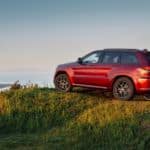 A red 2019 Jeep Grand Cherokee is parked atop a mountain overlooking a valley.