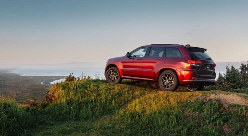 A red 2019 Jeep Grand Cherokee is parked atop a mountain overlooking a valley.