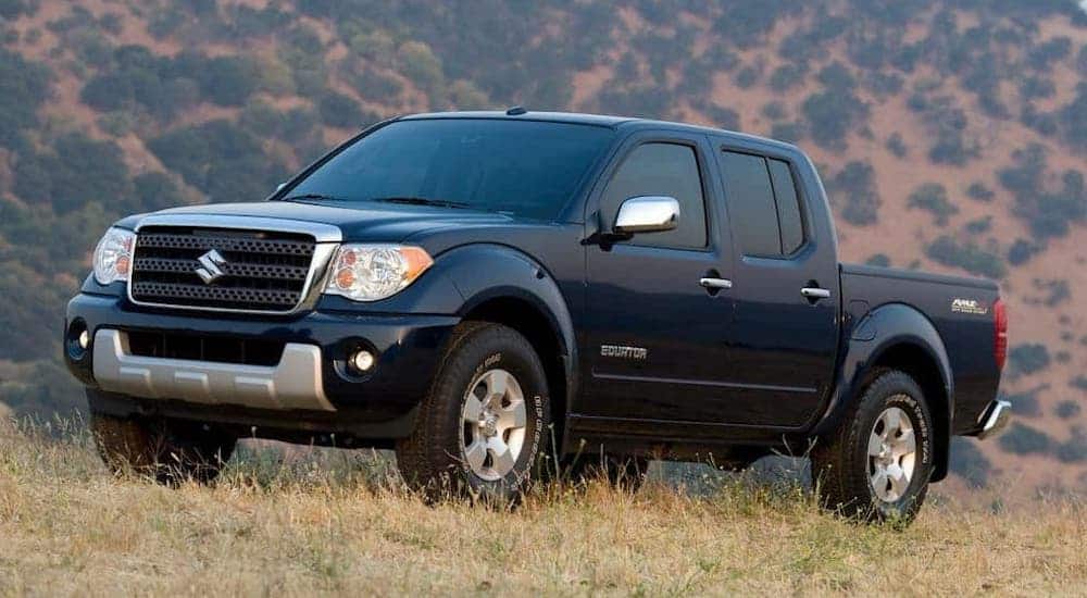A long forgotten used truck, a black 2009 Suzuki Equator is parked on a grassy hill.