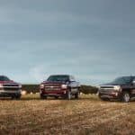 Three 2016 Silverado trucks are parked in a field.