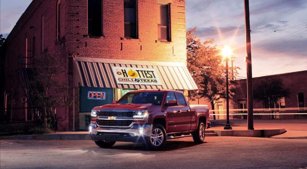 A red 2016 Chevy Silverado 1500 is parked in front of a restaurant at dusk.