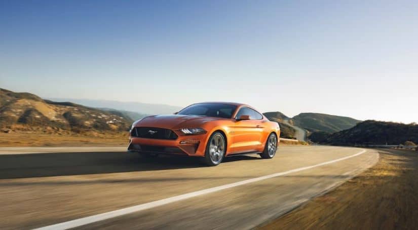 An orange 2018 Ford Mustang is driving on a winding mountain road.