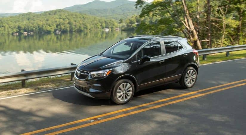 A black 2020 Buick Encore is driving past a lake after winning the 2020 Buick Encore vs 2020 Nissan Kicks comparison.