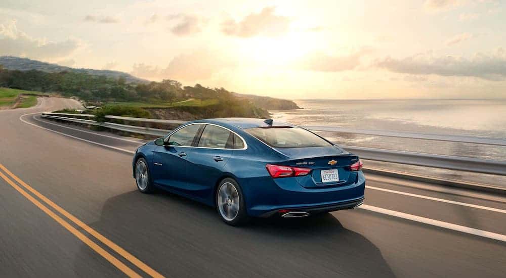 A blue 2020 Chevy Malibu is driving along a coastal highway after winning the 2020 Chevy Malibu vs 2020 Ford Fusion comparison.