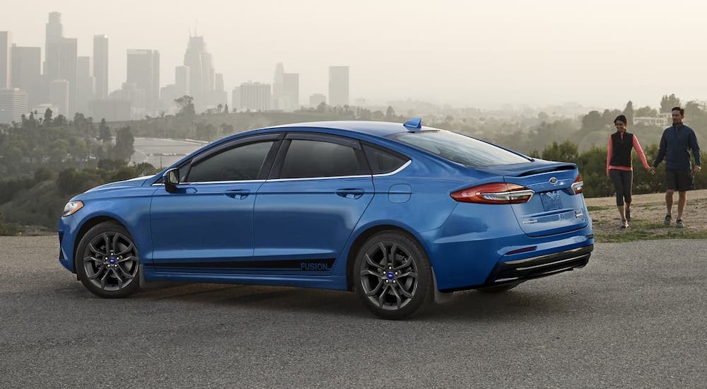 A blue 2020 Ford Fusion is parked with a hazy city in the distance.