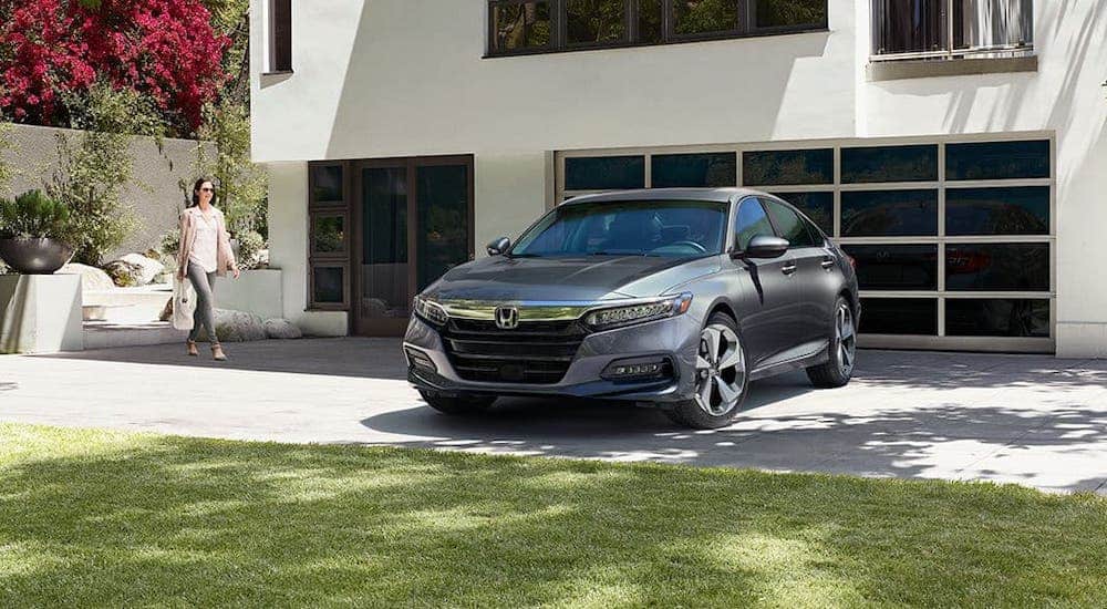 A woman is walking towards a gray 2020 Honda Accord Touring 2.0T that is parked in the driveway of a modern home.
