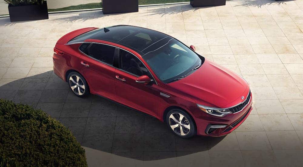 A red 2020 Kia Optima is parked on tan tiles and shown from above.