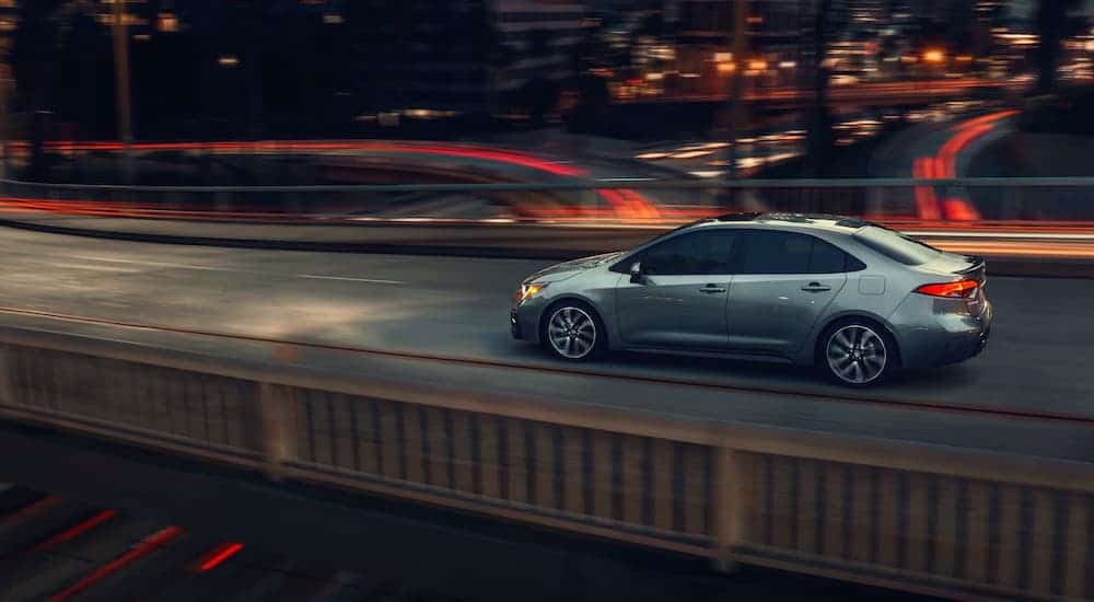 A gray 2020 Toyota Corolla is driving over a city highway at night.