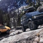 An orange 2-door and a dark blue 4-door 2021 Ford Bronco are off-roading on a mountain.