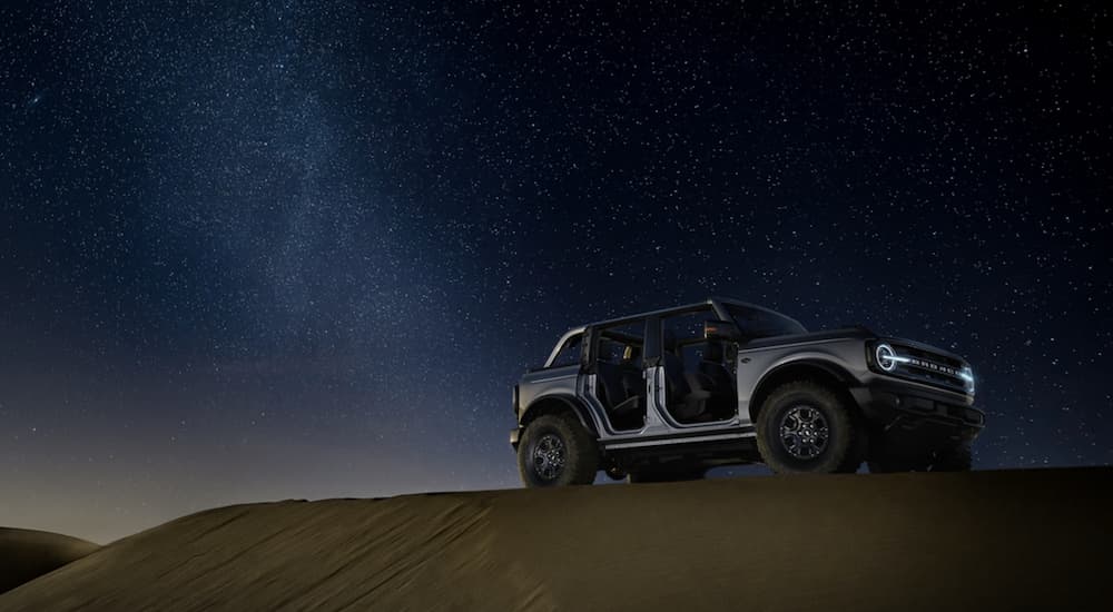 A silver 2021 Ford Bronco Wildtrak is parked under a starry night sky with no doors.
