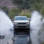 One of the best SUVs, a silver 2020 Jeep Cherokee, is shown from the front driving through a pond.