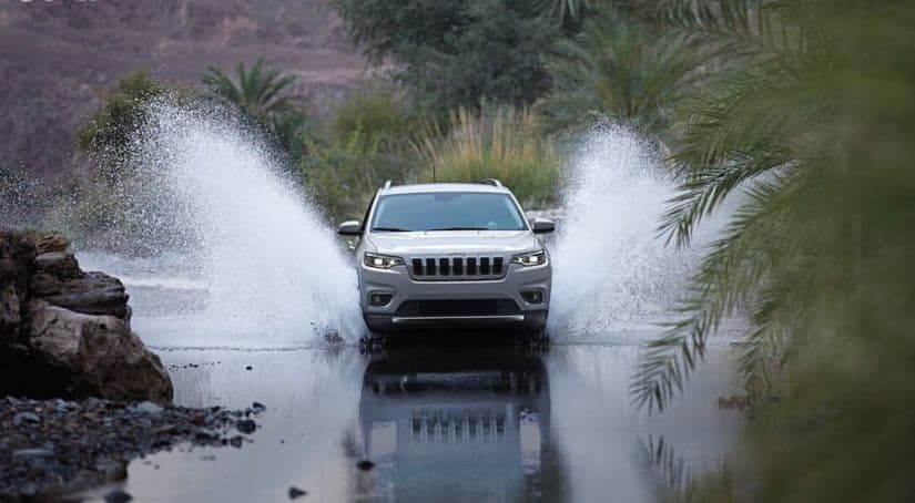 One of the best SUVs, a silver 2020 Jeep Cherokee, is shown from the front driving through a pond.