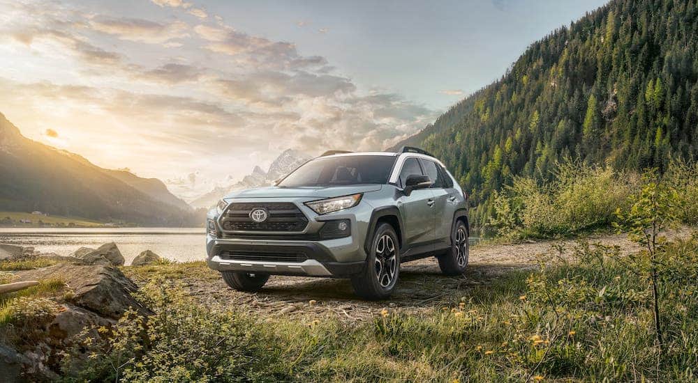 One of the best SUVs, a silver 2020 Toyota Rav4, is parked in front of a lake and mountain.