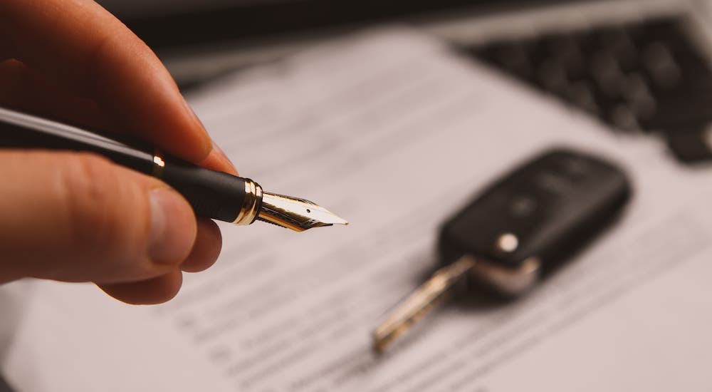 A closeup shows a pen in front of paperwork and a car key.