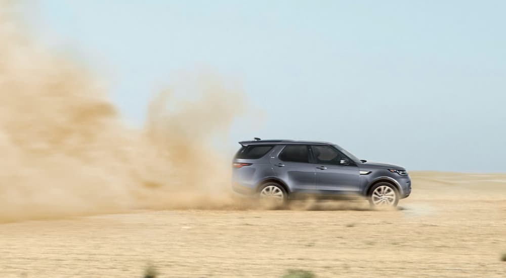 A blue 2020 Land Rover Discovery is kicking up dust while riving in sand.