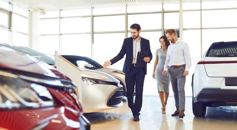 A salesman is showing a couple the vehicles at a local car dealership.