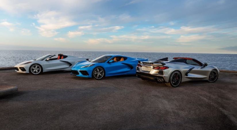 A white, a blue and a silver 2021 Chevy Corvette Stingray are parked in front of an ocean.