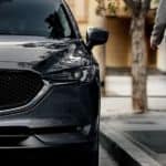 A closeup shows the front of a 2020 Mazda CX-5 and a woman walking towards it.