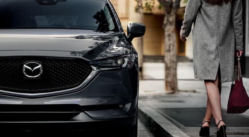 A closeup shows the front of a 2020 Mazda CX-5 and a woman walking towards it.