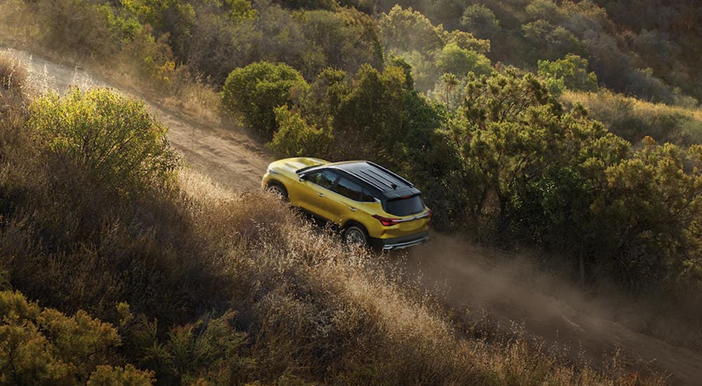 A yellow 2021 Kia Seltos is driving on a dirt road and shown from a high angle.