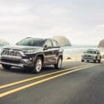 A black and a green 2020 RAV4 are driving on a coastal highway.