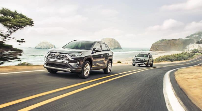 A black and a green 2020 RAV4 are driving on a coastal highway.