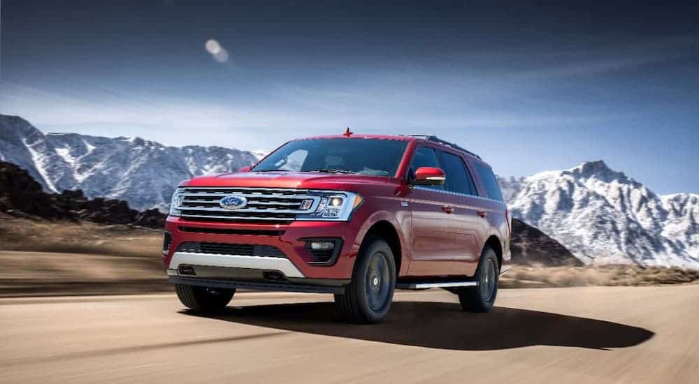 A red 2018 Ford Expedition is driving on a highway in front of snow-covered mountains.