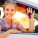 A woman is hanging out the window of a white car holding car keys.
