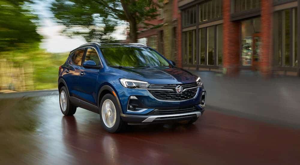 A blue 2020 Buick Encore GX is driving past a brick building.