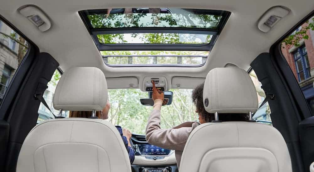 The white interior of a 2020 Buick Encore GX is shown as two people are in the front seat, opening the sun roof.