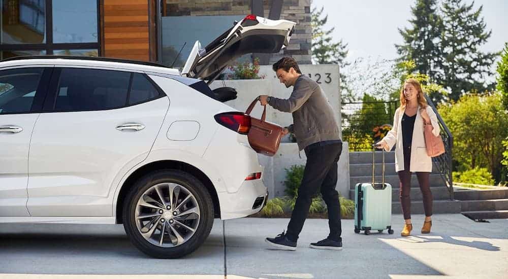 A couple is loading up luggage in the back of a white 2020 Buick Encore GX in front of a modern home.