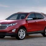 A red 2020 Chevy Equinox is parked in front of a low cement wall and sky after winning the 2020 Chevy Equinox vs 2020 Nissan Rogue comparison.