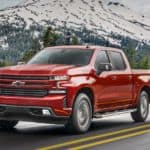 A red 2020 Chevy Silverado 1500 is driving past a snow capped mountain.