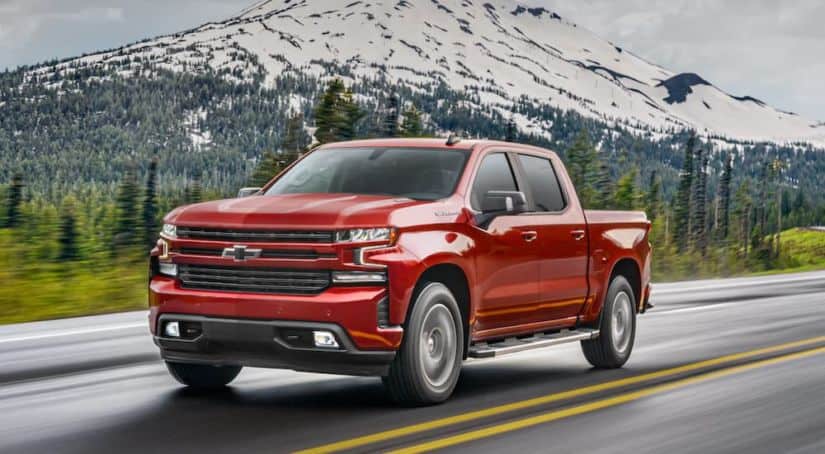 A red 2020 Chevy Silverado 1500 is driving past a snow capped mountain.