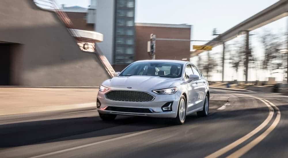 A white 2020 Ford Fusion is driving on a city street after winning the 2020 Ford Fusion vs 2020 Subaru Legacy comparison.