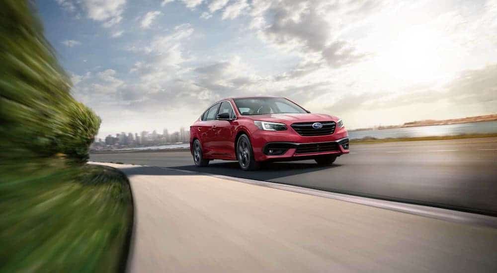 A red 2020 Subaru Legacy is driving around a corner away from a city.