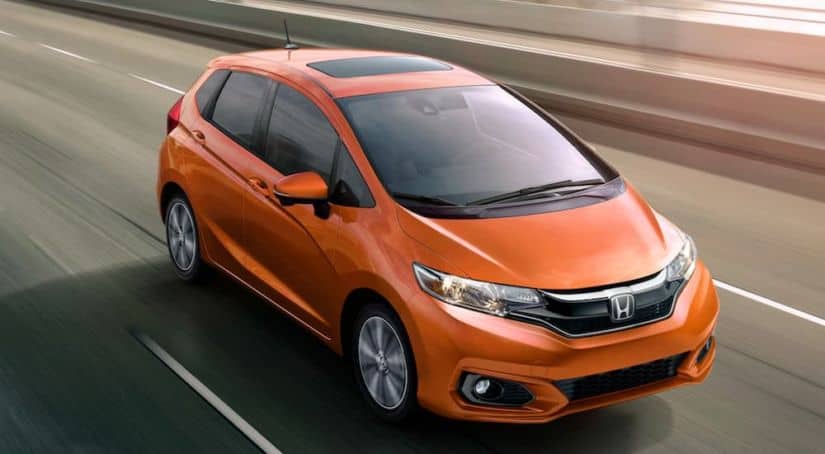 An orange 2020 Honda Fit is driving on a multi-lane highway.