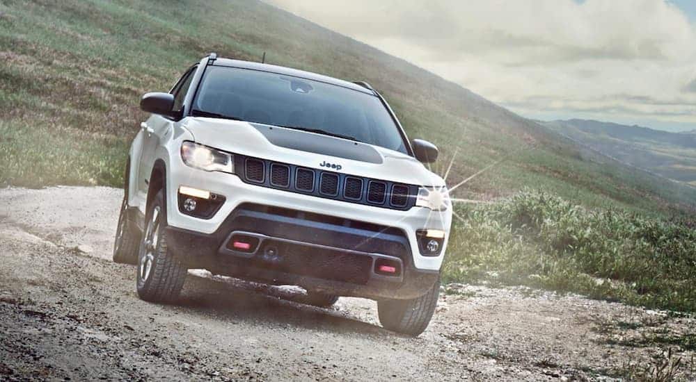 A white and black 2020 Jeep Compass is off-roading on a mountain trail with more mountains in the distance.