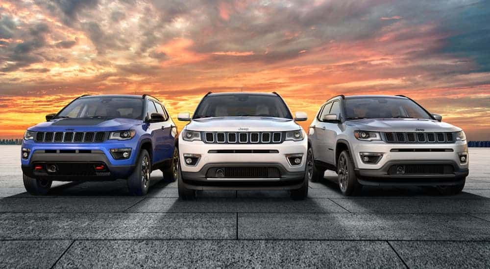A blue, a white, and a grey 2020 Jeep Cherokee are driving in a line in front of a sunset.