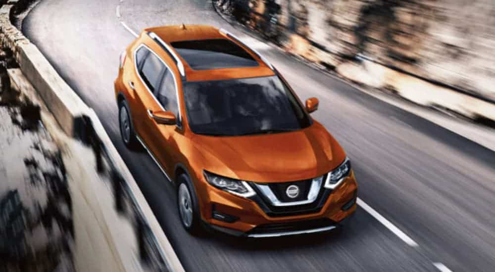 An orange 2020 Nissan Rogue is driving on a highway with two lanes.