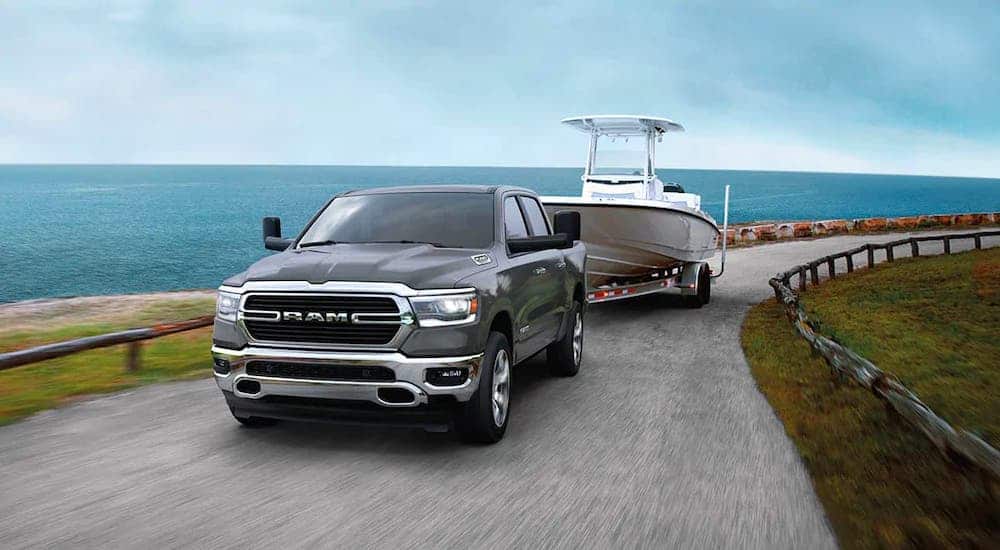 A gray 2020 Ram 1500 is towing a boat on a coastal highway.