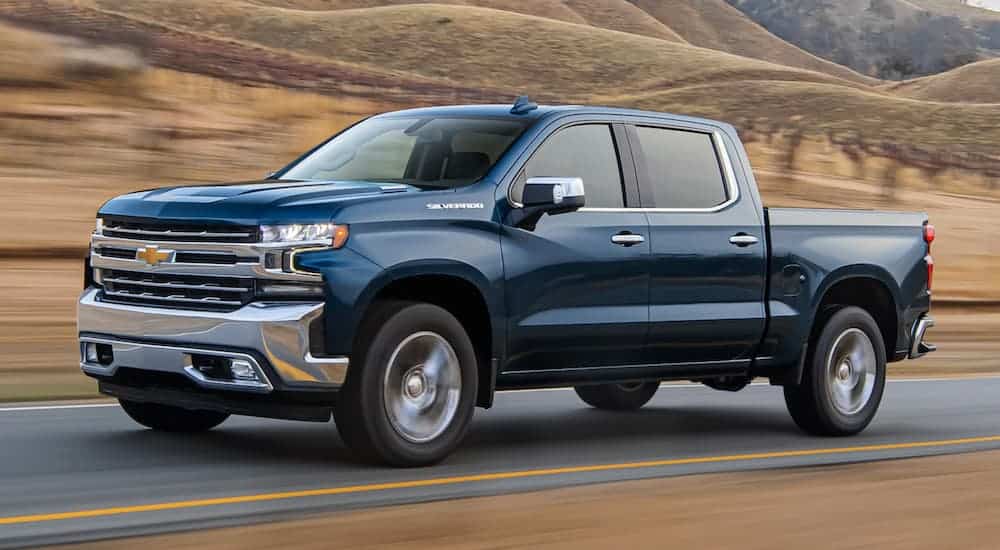 A blue 2020 Chevy Silverado 1500 is driving past dry grass on a hill.