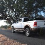 A white 2020 Ram 2500 is driving on a rural road in front of a large tree.