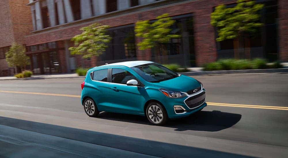 A teal 2021 Chevy Spark is driving on a city street.