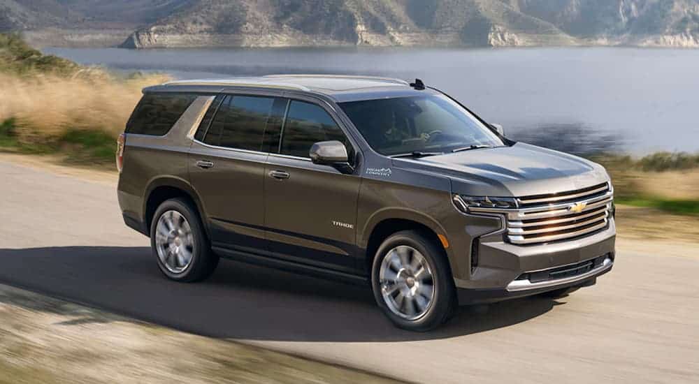 A grey 2021 Chevy Tahoe High Country is driving past a lake.