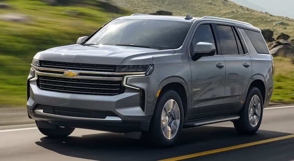 A grey 2021 Chevy Tahoe LT is driving past grassy hills.