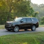 A brown 2021 Chevy Tahoe High Country is driving on a tree-lined road.