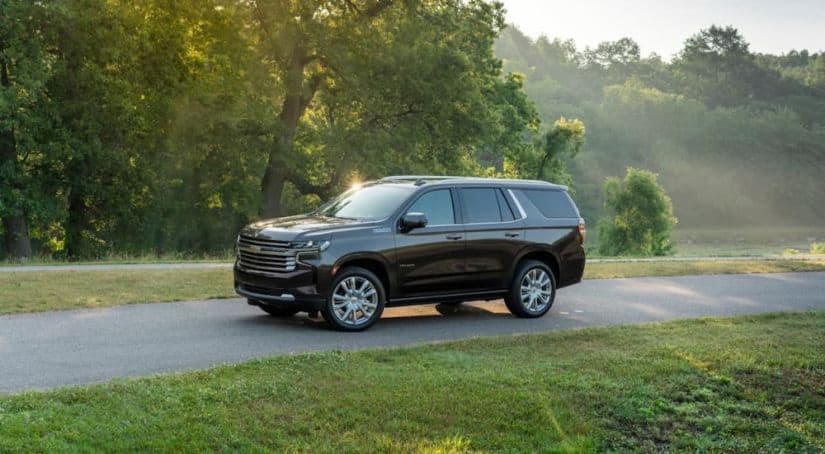 A brown 2021 Chevy Tahoe High Country is driving on a tree-lined road.