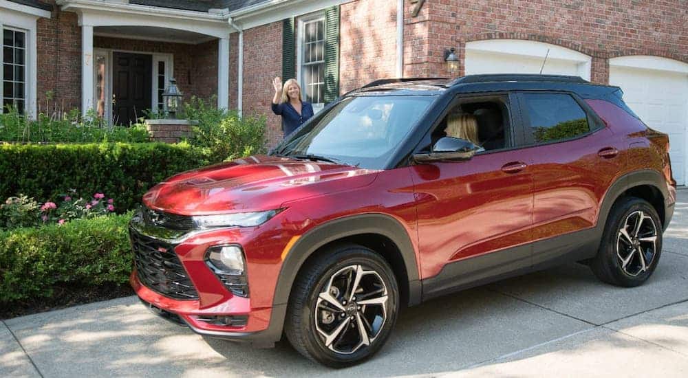 A mother is waving to her daughter who is leaving the driveway in a red 2021 Chevy Trailblazer.